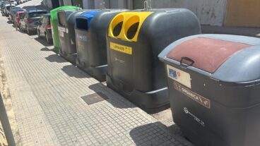 Fila de contenedores de reciclaje de distintos colores en una acera de Benissa, con el contenedor marrón de orgánica en primer plano.