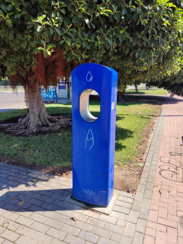 Compromís per Pego exige regular el área de autocaravanas y denuncia su abandono 2 Imagen: Fuente de agua azul en una zona de parque y paseo pavimentado en Pego.