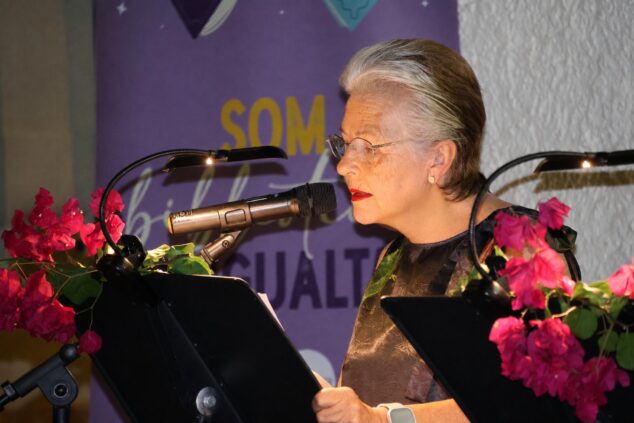 Imagen: Fotografía de una mujer leyendo en un micrófono durante un acto literario al aire libre en Benitatxell.