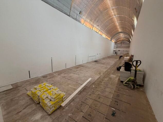 Imagen: Vista interior del Trinquet Municipal de Benissa con materiales de obra y un operario trabajando en la renovación del suelo.