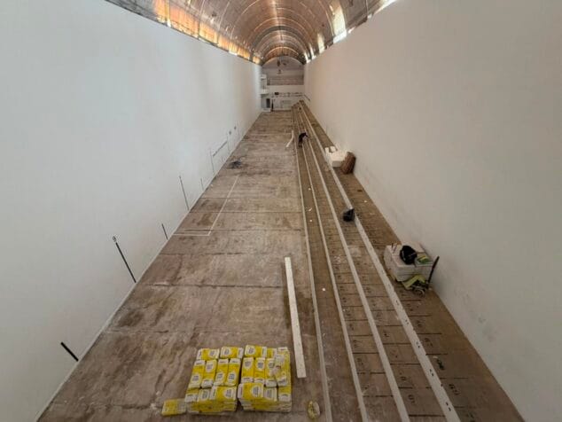 Imagen: Fotografía del interior del Trinquet Municipal de Benissa en obras, con sacos de material y operarios trabajando en la renovación del suelo.
