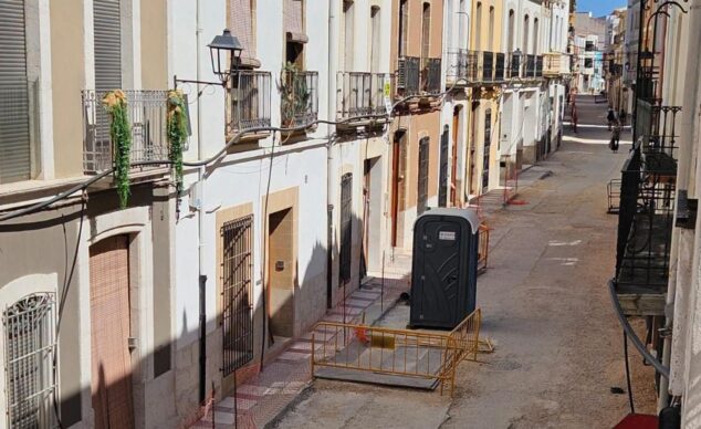 Las obras en la calle La Bassa de Gata de Gorgos se reanudan tras el hallazgo de los restos arqueológicos 1 Imagen: Una calle en Gata de Gorgos en obras, con el suelo de tierra, vallas amarillas y un baño portátil al fondo.