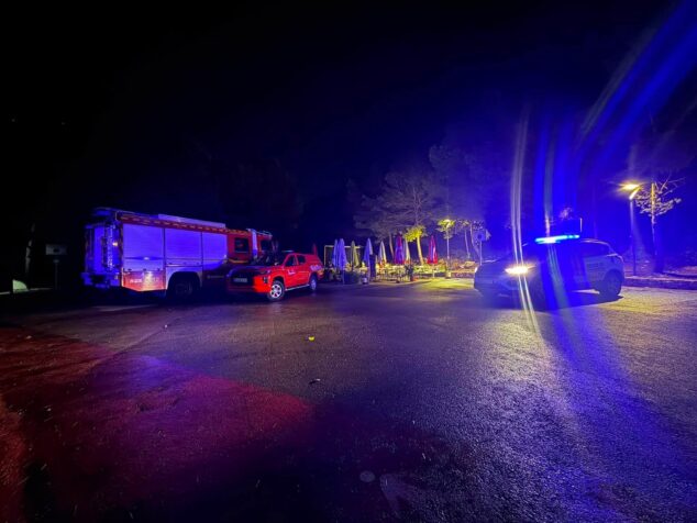 Vista nocturna de vehículos de emergencia, incluyendo un camión de bomberos y un coche de policía con luces azules parpadeantes, estacionados durante una intervención de rescate en Benitatxell.