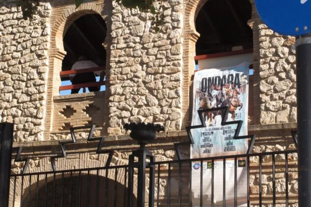 Fachada de piedra de la plaza de toros de Ondara con un gran cartel anunciando una feria taurina.
