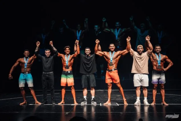 Atletas y organizadores de culturismo celebrando en un podio tras una competición.