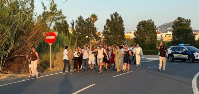 Pamis despide sus fiestas patronales a Sants de la Pedra con gran participación y convivencia 12 Grupo de personas caminando por una carretera al atardecer, llevando una anda decorada y precedidos por un coche de policía local.