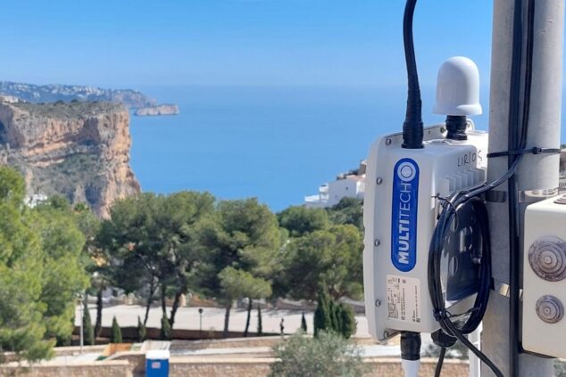 Imagen: Primer plano de un dispositivo sensor MultiTech montado en un poste con el paisaje costero y acantilados de Benitatxell al fondo bajo un cielo azul.