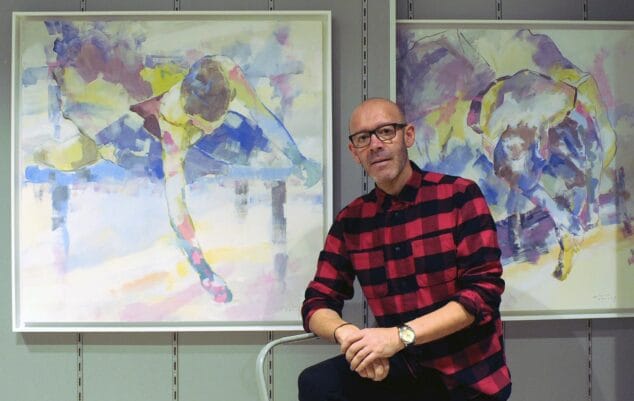 Ondara anuncia sus tres distinguidos 9 d'Octubre 2026: Josep Andreu Alemany, Antonio Torres y Sergi Mallol 1 Imagen: El artista Antonio Torres Alba posa con gafas y camisa de cuadros delante de dos pinturas abstractas.