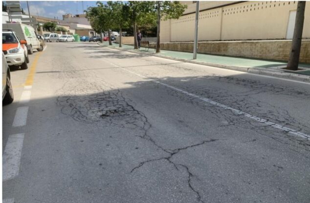 Imagen: Fotografía de una calle asfaltada con grandes baches y grietas profundas en el centro de la calzada en una zona residencial de Calp.