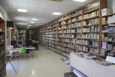 Pedreguer abre la convocatoria de ayudas para estudios superiores y material escolar 2026-2027 7 Vista del interior de la biblioteca municipal de Pedreguer con estanterías llenas de libros, mesas de estudio con ordenadores y un mostrador de préstamo.
