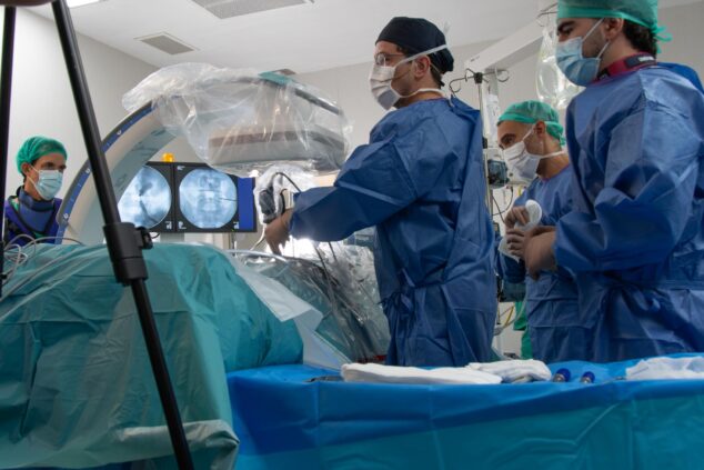 Imagen: Equipo médico en un quirófano del Hospital de Dénia durante una cirugía de columna mínimamente invasiva, con monitores mostrando imágenes.