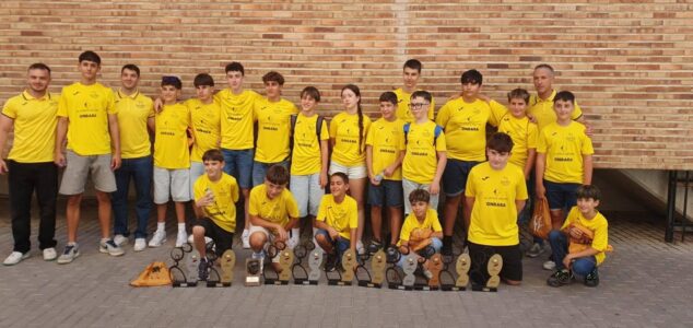 La Escuela Municipal de Pilota d’Ondara cosecha una exitosa temporada 2025-26 con diez galardones autonómicos 2 Imagen: Grupo de jóvenes y adultos de la Escuela de Pilota de Ondara con camisetas amarillas posando con varios trofeos frente a una pared de ladrillo.