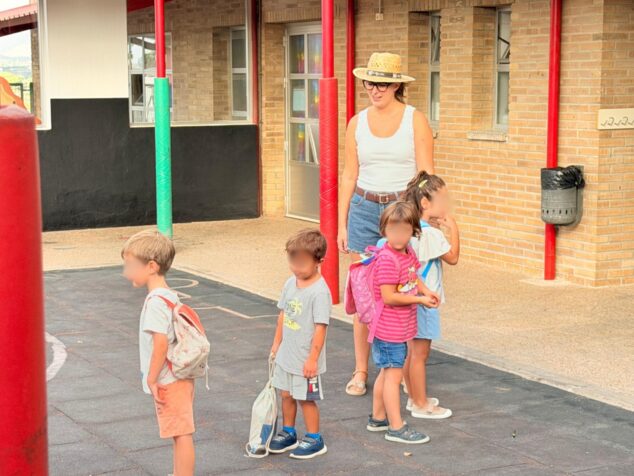 Varios niños pequeños con mochilas y una mujer adulta en el patio del colegio CEIP Santa María Magdalena.