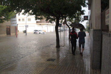 jovenes bajo el paraguas junto a una avenida anegada de denia durante un episodio de lluvia torrencial