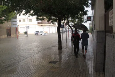 Jóvenes bajo el paraguas junto a una avenida anegada de Dénia durante un episodio de lluvia torrencial