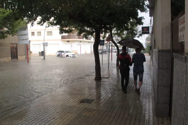 jovenes bajo el paraguas junto a una avenida anegada de denia durante un episodio de lluvia torrencial