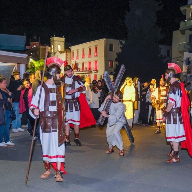 Imagen: Actores vestidos de soldados romanos escoltan a un hombre representando a Jesús cargando la cruz en una procesión nocturna.