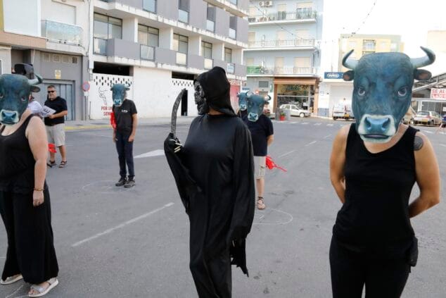 Varios activistas con máscaras de cabeza de toro y una persona disfrazada de la Muerte con una guadaña participan en una protesta en una calle de Ondara.