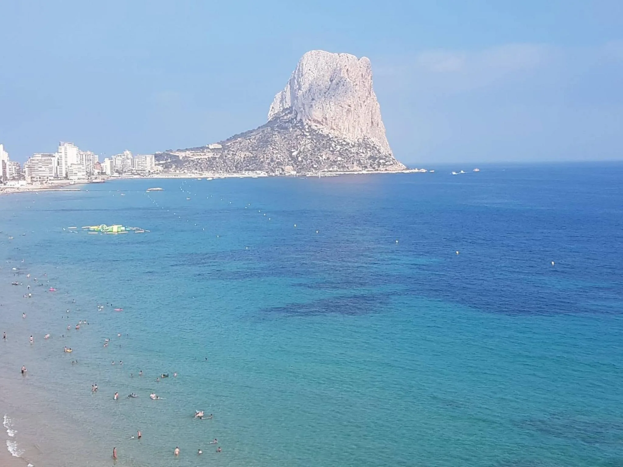 Vista panorámica de una playa de Calp con bañistas en el agua azul turquesa y el Peñón de Ifach al fondo.