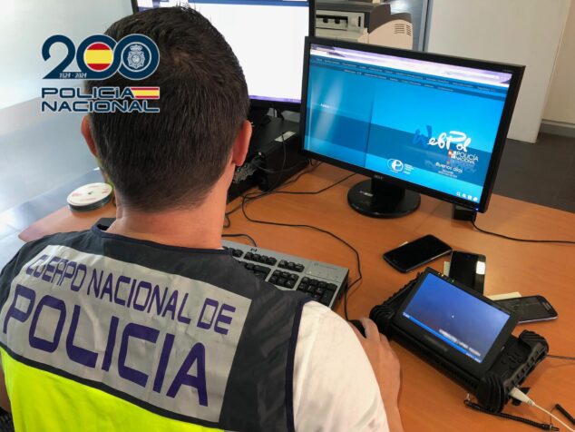 Alertan de un nuevo método de estafa donde los ciberdelincuentes suplantan cuentas de WhatsApp 1 Imagen: Un agente de la Policía Nacional de espaldas frente a dos monitores de ordenador y varios teléfonos móviles en una mesa de oficina.