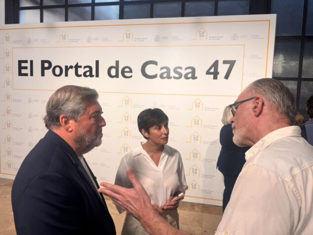 Imagen: Tres personas conversan de pie frente a un gran cartel que anuncia "El Portal de Casa 47" y logotipos oficiales.