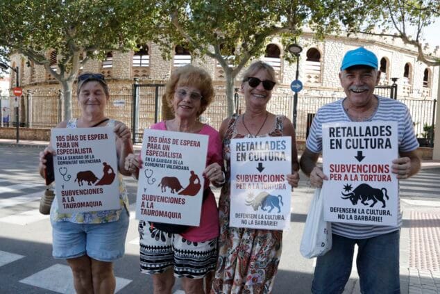 Cuatro personas mayores sostienen carteles de protesta contra la tauromaquia y sus subvenciones frente a una plaza de toros.