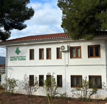 Fachada blanca del edificio de la Mancomunidad Alto Turia con su logotipo y nombre en verde.