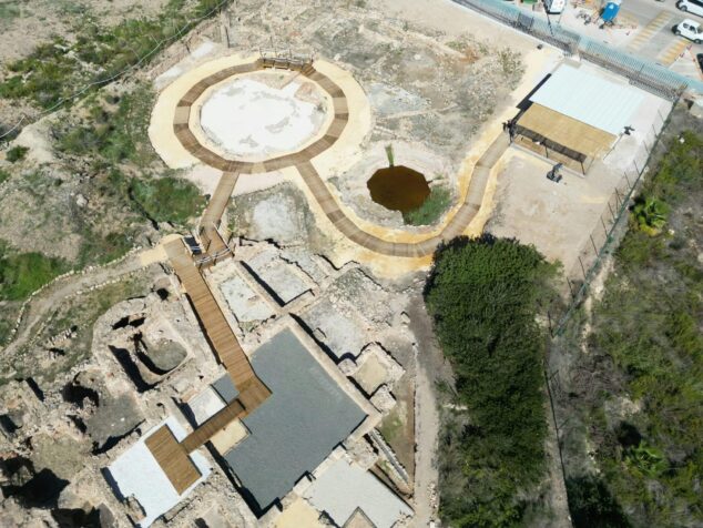 El impacto cultural de los Baños de la Reina: el yacimiento romano de Calp atrae a miles de turistas en un año 1 Imagen: Fotografía aérea del yacimiento arqueológico romano Baños de la Reina en Calp, mostrando ruinas, una estructura circular y pasarelas de madera para el recorrido de visitantes.