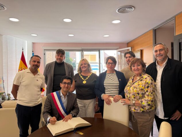 Calp explora un hermanamiento con la ciudad francesa de Neuilly-sur-Marne 1 Imagen: El alcalde francés Zartoshte Bakhtiari firma un libro, observado por la alcaldesa Ana Sala y otros miembros de la delegación en una oficina.