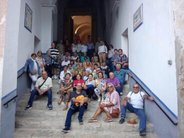 Gran grupo de personas mayores de Benitatxell posando en unas escaleras de piedra durante una salida cultural.