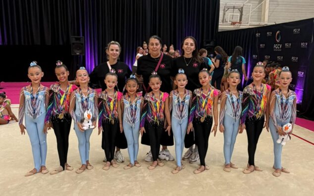 Imagen: Grupo de jóvenes gimnastas del Club Les Marines con sus medallas y tres entrenadoras posando en un tapiz de competición.