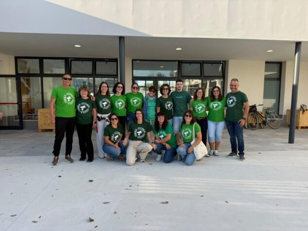 Imagen: Fotografía de grupo de trece docentes con camisetas verdes frente a la entrada del colegio CEIP Ausiàs March en Els Poblets durante una concentración.