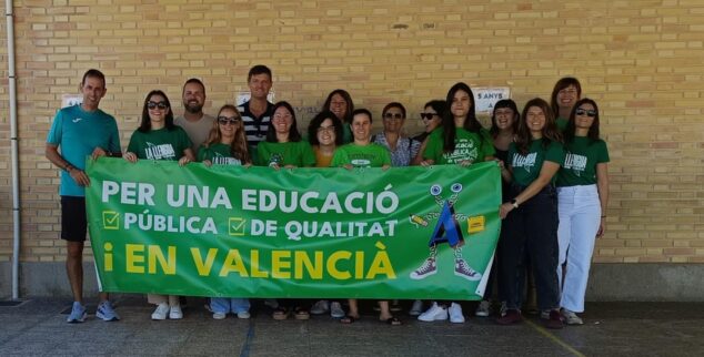 Imagen: Grupo de docentes posando con una pancarta verde que dice "PER UNA EDUCACIÓ PÚBLICA DE QUALITAT I EN VALENCIÀ" frente a un edificio de ladrillo.