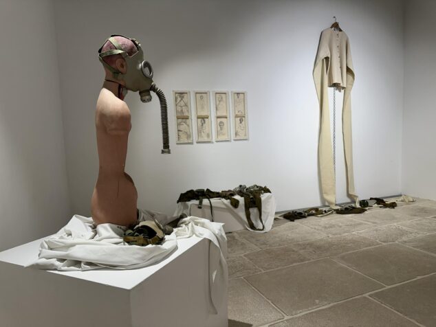 Imagen: Escultura de un torso con máscara de gas y otras obras en una sala de exposiciones.