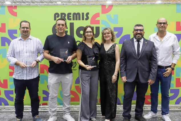 Imagen: Seis personas, tres de ellas sosteniendo trofeos, posan frente a un fondo verde con el logotipo de los Premis Clau.