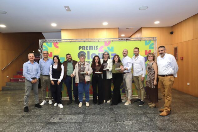 El Verger entrega sus II Premis Clau y homenajea a Elvira Salort por toda una vida dedicada al comercio 1 Imagen: Grupo de personas, incluyendo galardonados con trofeos y autoridades, posando delante de un photocall verde de los Premis Clau.