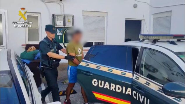 Imagen: Un guardia civil uniformado lleva a un hombre esposado y con la cara pixelada hacia un coche patrulla de la Guardia Civil.