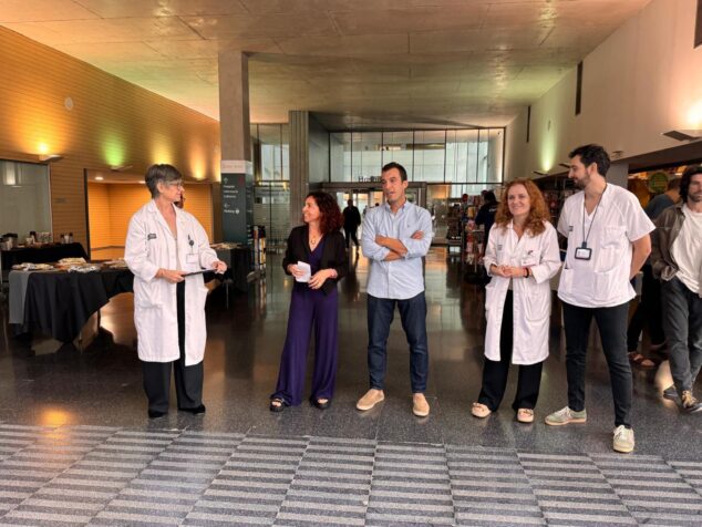 Imagen: Varias personas, incluyendo profesionales con batas blancas, de pie en el vestíbulo del Hospital de Dénia junto a mesas informativas.