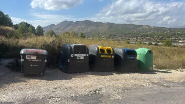 Benissa reduce la fracción resto hasta un 17,3 % con la implantación de los contenedores inteligentes 8 Fila de contenedores de reciclaje de distintos colores (marrón, gris, amarillo, azul, verde) situados en un entorno rural de Benissa con una montaña al fondo.