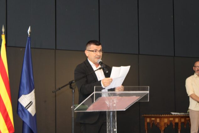 Cultura, historia y danza protagonistas en la celebración del 9 d’Octubre en Ondara 6 Imagen: Josep Andreu Alemany Ortolà hablando en un atril con un micrófono y papeles en la mano durante el acto de entrega de distinciones del 9 de Octubre en Ondara.