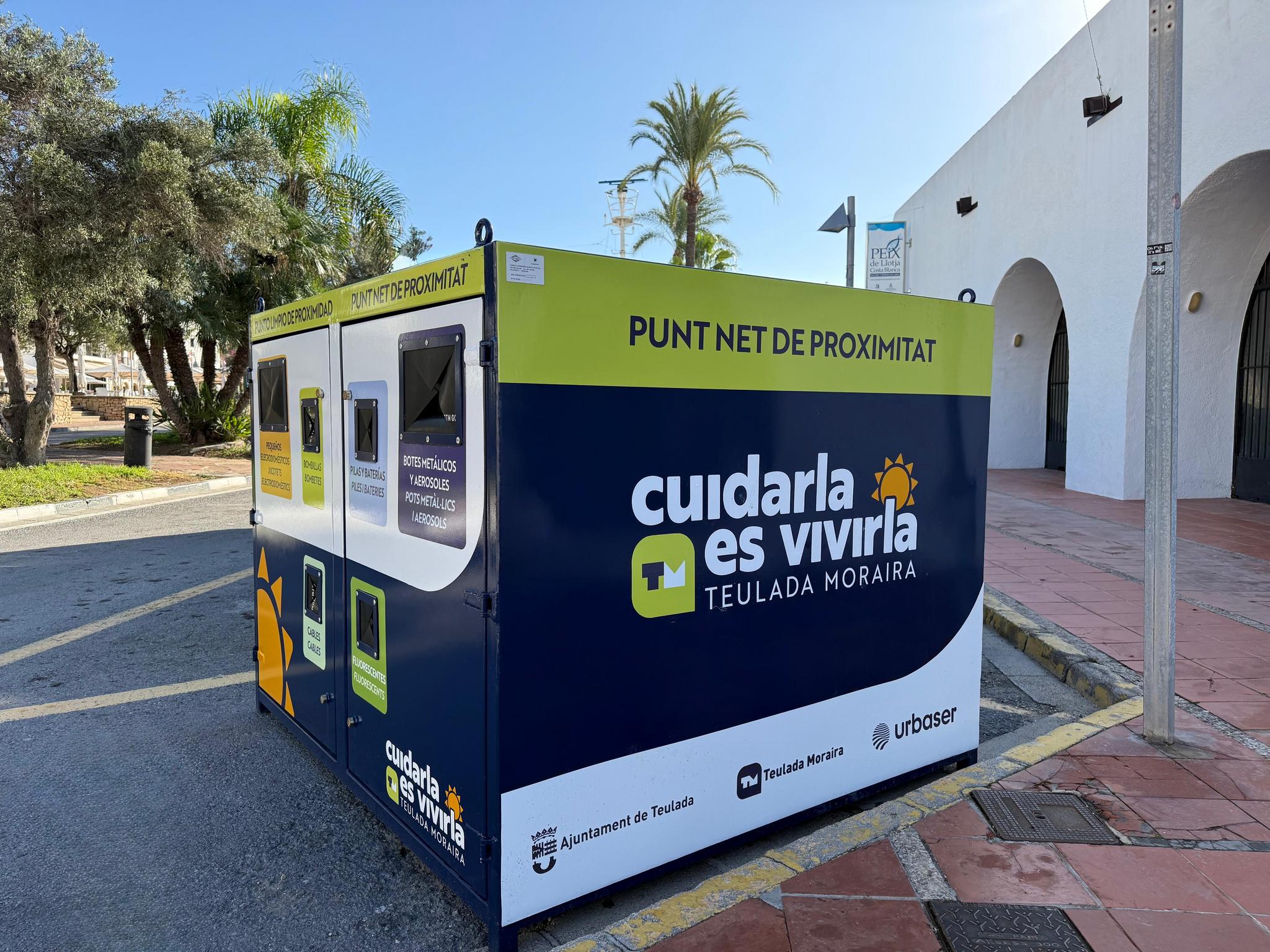 Punto limpio de proximidad azul y verde en Teulada Moraira, con el lema "Cuidarla es vivirla" y compartimentos para depositar distintos tipos de residuos.