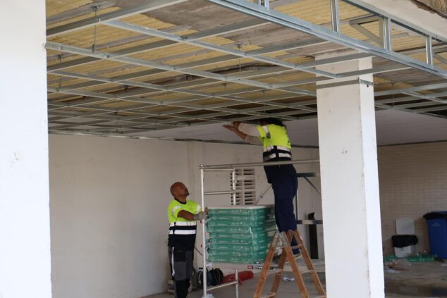 Imagen: Dos trabajadores de la construcción instalando paneles de falso techo en una estructura de hormigón.