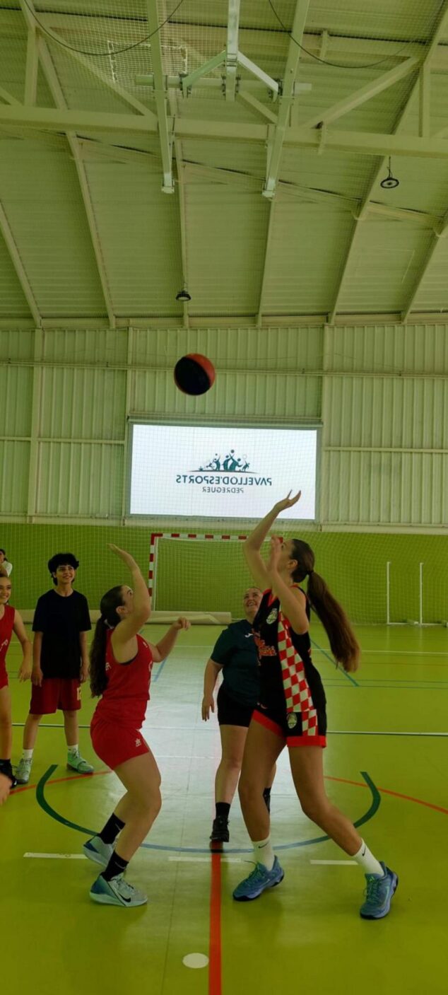 Imagen: Dos mujeres jóvenes jugando un partido de baloncesto en un pabellón interior, con una de ellas lanzando el balón.