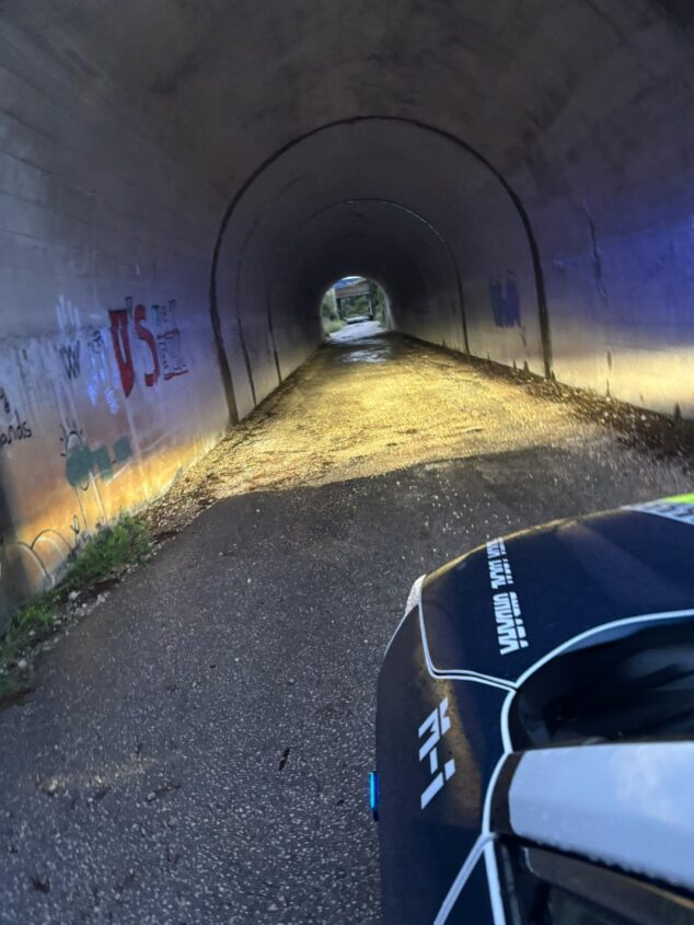 Imagen: Un coche de policía con las luces encendidas frente a la entrada de un túnel oscuro y con el suelo mojado e inundado.