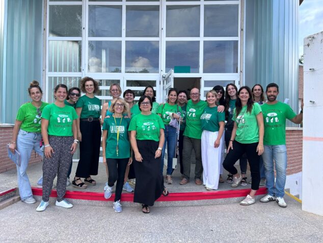 Imagen: Grupo de docentes con camisetas verdes reivindicativas posando frente a la entrada de un colegio público.