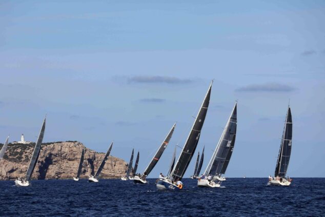 Imagen: Veleros navegando en una regata con una isla y un faro al fondo.